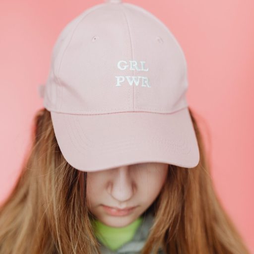 Portrait of a teenage girl in a pink 'Grl Pwr' cap on a matching background.